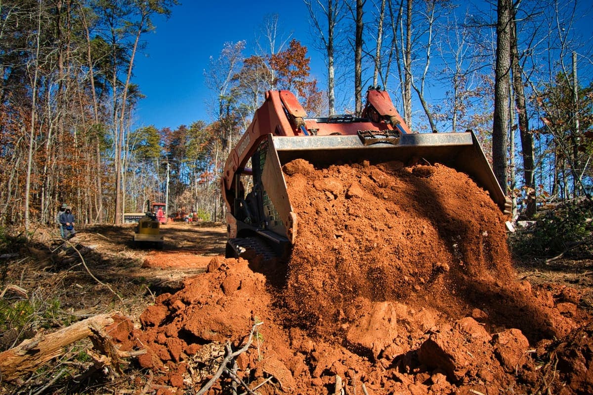 Compact track skid steer moving dirt on a wooded job site