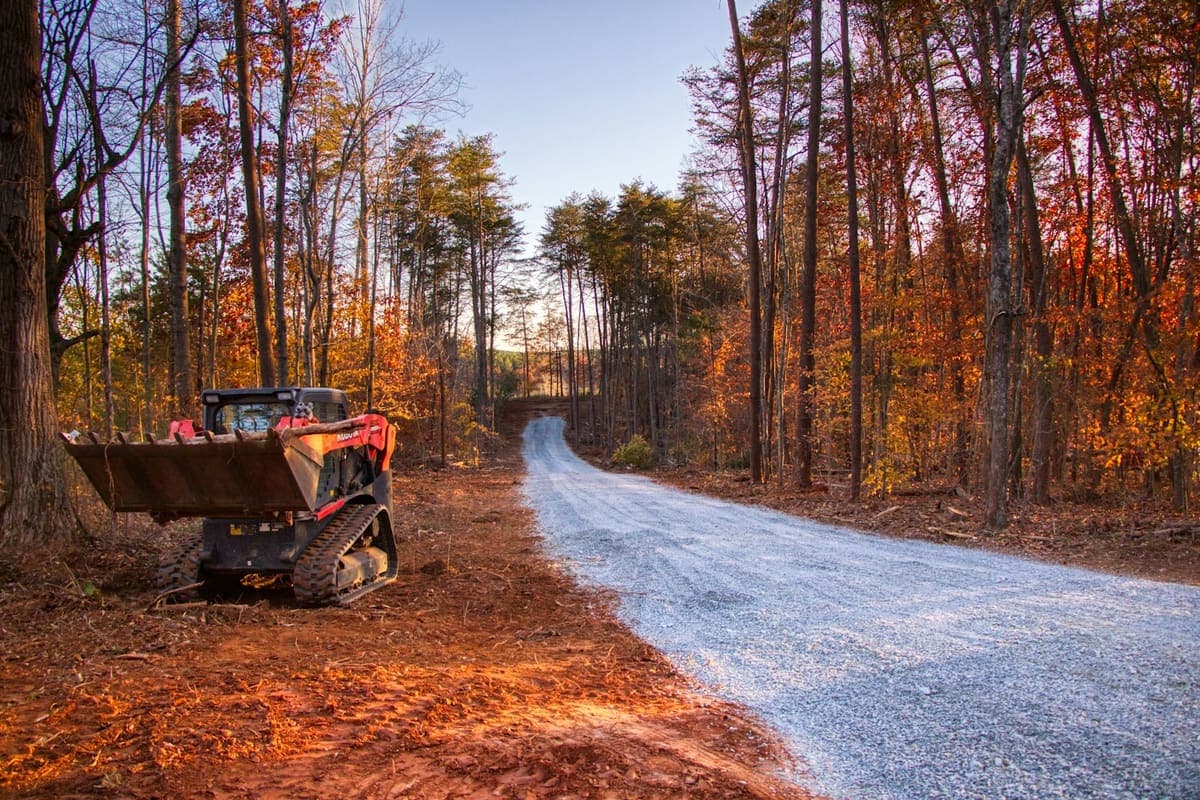 Freshly graded gravel driveway through a wooded property